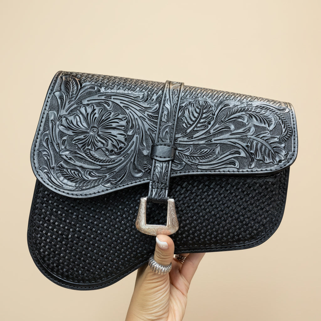 Black leather handbag with intricate silver tooled design held by a hand.