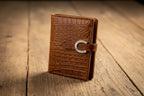 Brown leather wallet held by a hand against a gray background