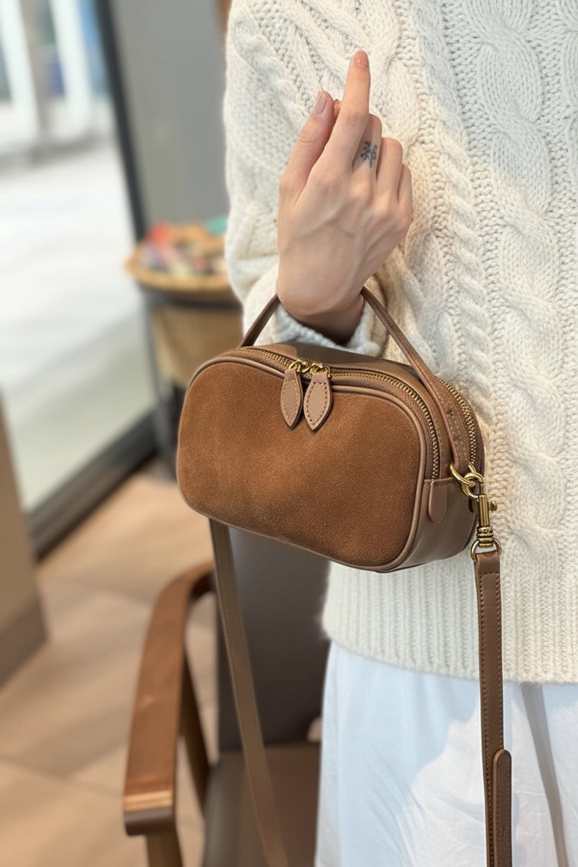 Brown handbag held by a person wearing a patterned sweater indoors.