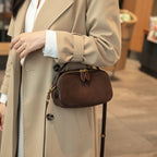 Brown handbag held by a person wearing a gray sweater.