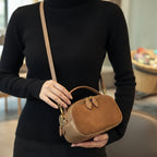 Brown suede handbag worn over shoulder with a patterned sweater and blurred indoor background