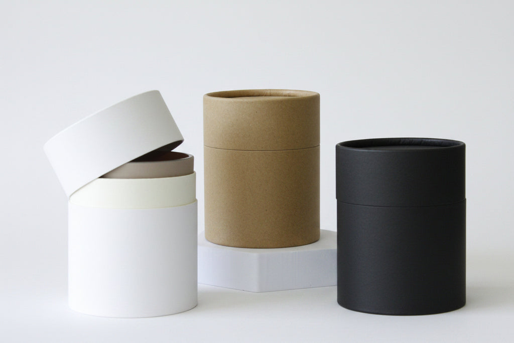 Four cylindrical planters in white, beige, brown, and black on a neutral background - Candle Jar Tube Packaging
