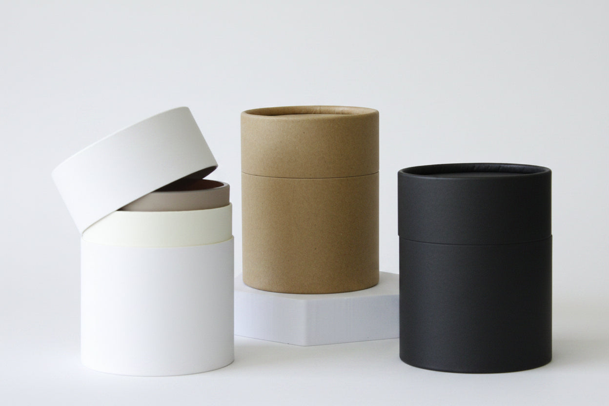 Four cylindrical planters in white, beige, brown, and black on a neutral background - Candle Jar Tube Packaging