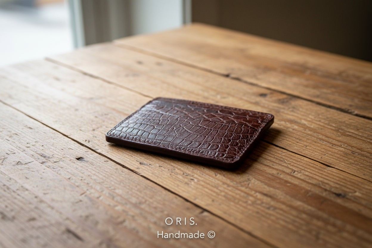 Brown leather cardholder with crocodile texture on a light gray background, featuring the brand 'ORIS'.