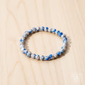 Beaded bracelet with blue and white stones on a reflective surface with pink flowers in the background