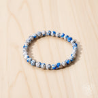 Beaded bracelet with blue and white stones on a reflective surface with pink flowers in the background