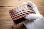 Handmade brown leather cardholder held by a gloved hand on a neutral background