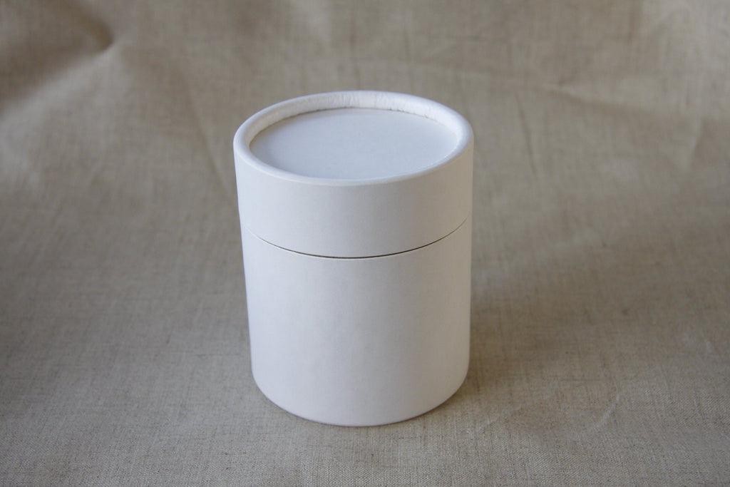 White cylindrical container with a lid on a beige fabric background