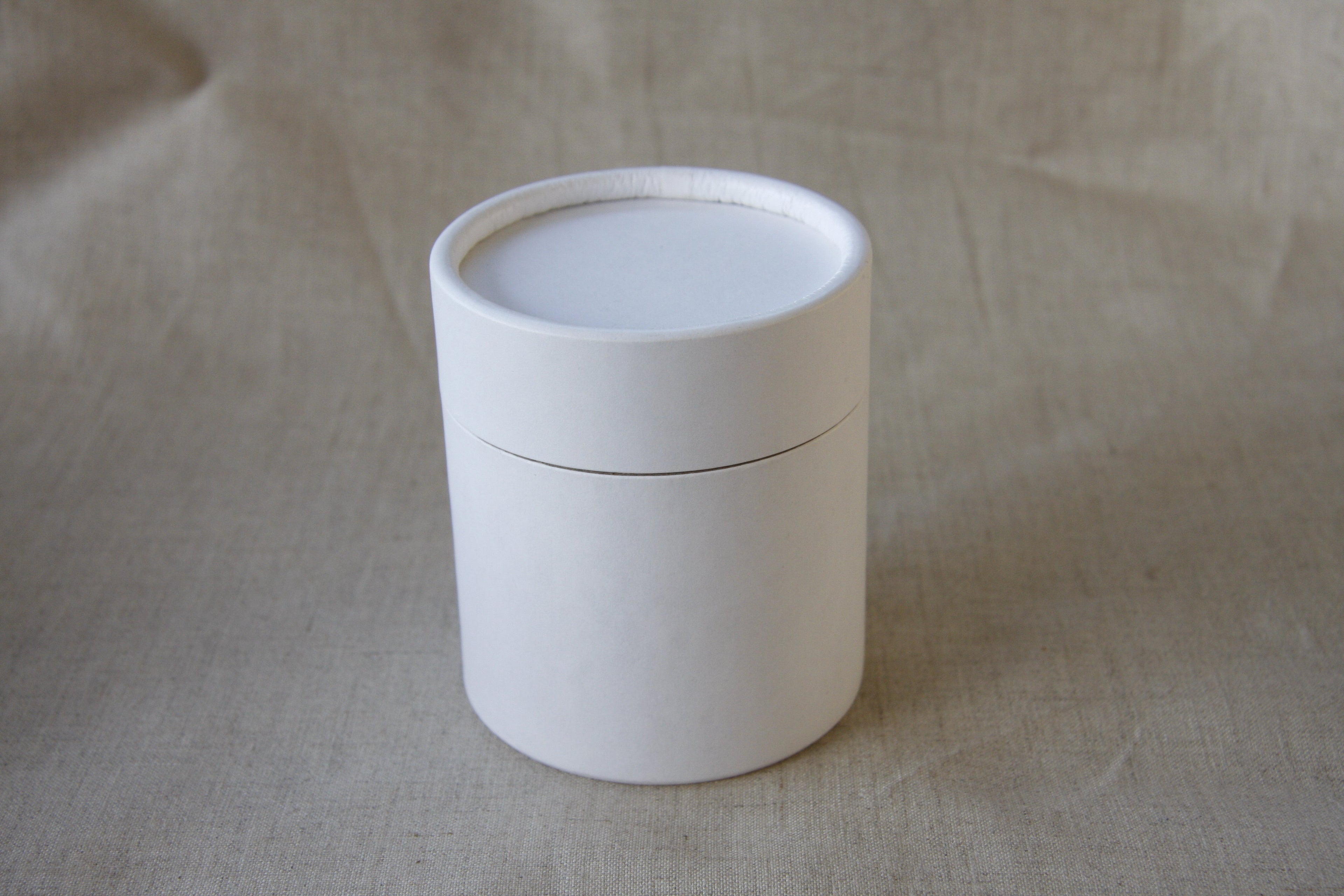 White cylindrical container with a lid on a beige fabric background