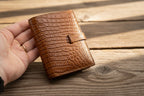 Brown leather wallet held in a hand against a light gray background