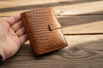Brown leather wallet held in a hand against a light gray background