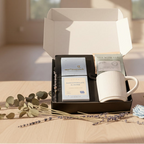 corporate gift package having Tea package, mug, and chocolate bar on a wooden surface with flowers.