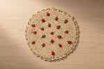 Round woven placemat with red berry patterns on a plain background