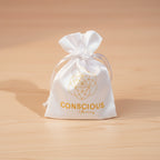 Colorful beaded bracelet on a teal box with 'Conscious' branding, flowers, and a bag in the background.