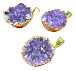 Three purple crystal pendants with gold bases on a wooden surface