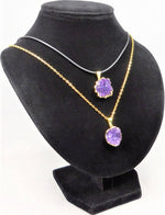 Two gold necklaces with purple pendants on a black velvet stand.
