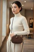 Brown handbag held by a person wearing a gray sweater.