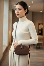 Brown handbag held by a person wearing a gray sweater.