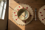Woven placemat with decorative red berries on a wooden table with a plate and fork.