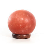 Himalayan Salt Rock sphere on a wooden stand against a white background