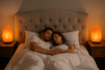 Couple lying in bed together with warm lighting from salt lamps.
