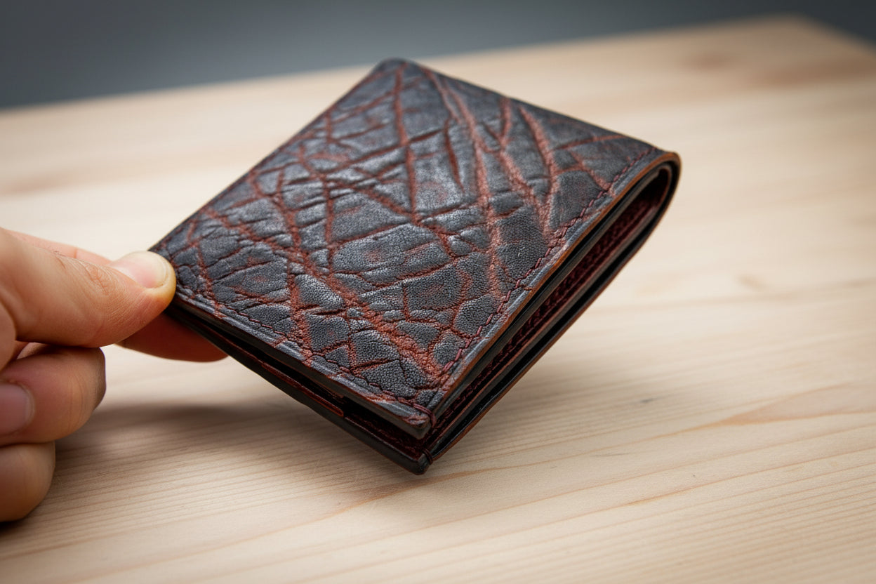 Brown leather wallet with embossed pattern held by a hand on a wooden surface