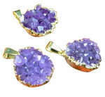 Three purple geode-style pendants with gold accents on a wooden surface