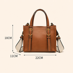 A brown leather handbag with a beige and white shoulder strap, with dimension lines