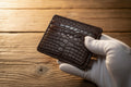 Brown leather cardholder with embossed texture held by a gloved hand on a wooden surface, with 'O.R.I.S. Handmade' branding.